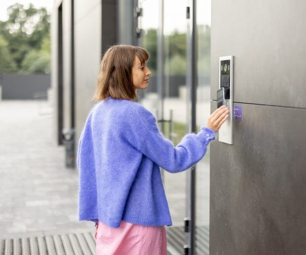Young stylish woman getting access to the building by attaching smartphone to intercom